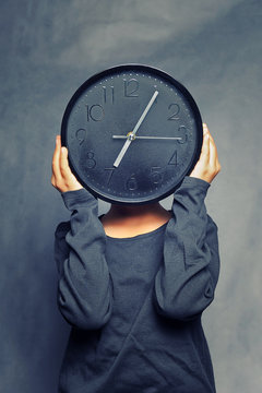 Young Child Holding Clock In Front Of Head