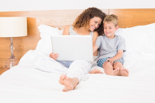 Mother and son sitting on bed using laptop