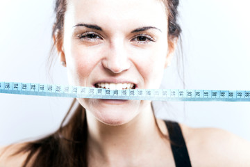 Angry young woman biting measuring tape