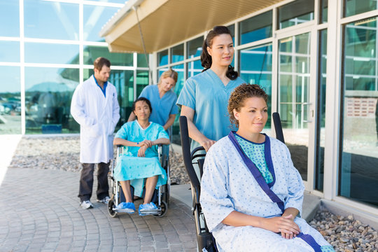 Nurses Assisting Patients On Wheelchairs Outside Hospital Buildi