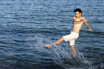 Young man splashing water at the beach, tourist