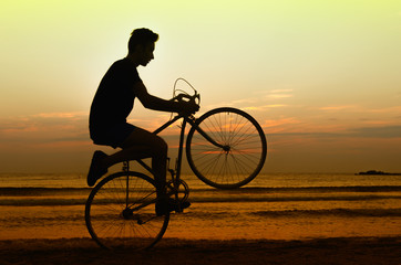 Fototapeta premium Man riding a bicycle at the sunrise on the beach, getting fit
