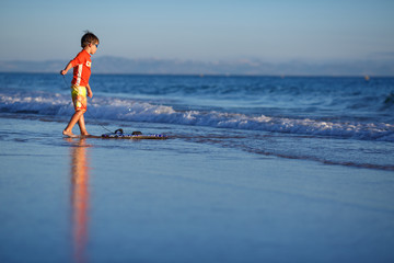 Six years old boy with surf board on exotic beach