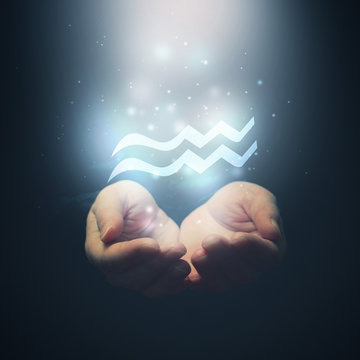 Female hands opening to light and holding zodiac sign for Aquari