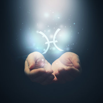 Female hands opening to light and holding zodiac sign for Pisces