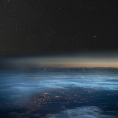 The Earth at night. City lights below the clouds, stars above.