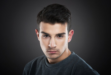 Fototapeta premium Serious young man looking at camera, dark background