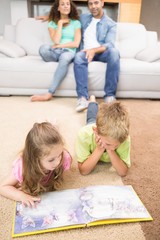 Happy siblings lying on the rug reading a storybook