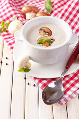 Mushroom soup in white pot, on napkin, on wooden background