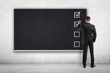 businessman drawing checklist on blackboard
