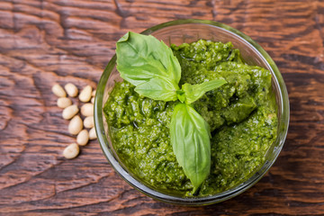 Fresh pesto in small glass bowl on wooden background
