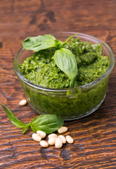 Fresh pesto in small glass bowl on wooden background