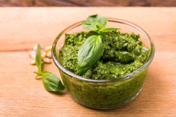 Fresh pesto in small glass bowl on wooden background
