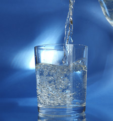 Pour water from  pitcher into  glass, on dark blue background