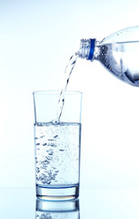 Pour water from bottle into  glass, on light blue background