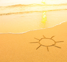 Sun drawn in the sand of a beach, soft surf wave.