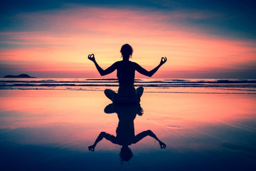 Fototapeta na wymiar Yoga woman sitting on sea coast at sunset.