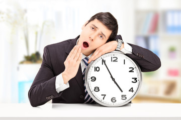 Sleepy young businessman leaning his head on a big wall clock