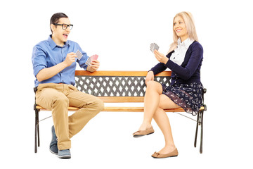Fototapeta premium Young couple playing cards seated on wooden bench