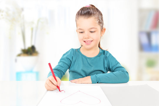 Young child drawing hearts on a piece of paper, indoors