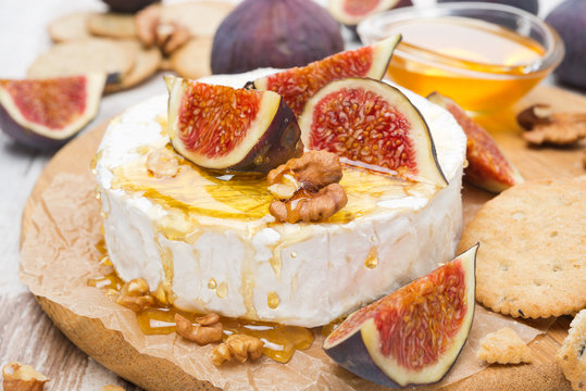 Camembert cheese with honey, figs and crackers on a wooden board