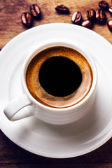 Coffee cup with white saucer and roasted coffee beans  on wooden