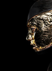 Woman's Face Covered Golden Foil over Black Background. Mystery
