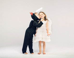 Little devil-boy kissing his angel friend