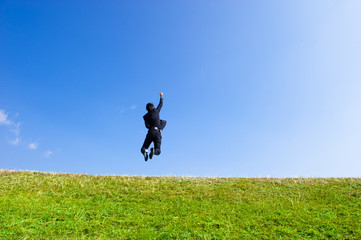 青空に向かって大きくジャンプするスーツの男性