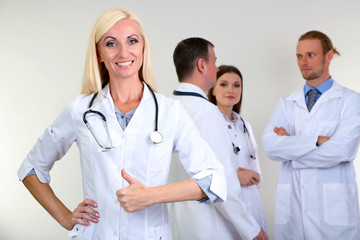 Fototapeta premium Doctor standing in front of coworkers on grey background