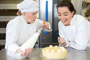 Confectioner apprentice nibbling whipped cream from cake