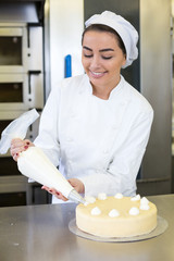 Baker prepares cake in bakehouse with whipped cream