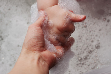 Fototapeta premium kid hand holding her mother's hand in the bath with foam