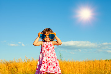 Happy little girl with big sunglasses in the wheat field