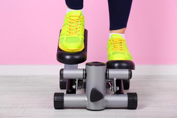 Woman doing exercise on stepper. Close-up on legs.