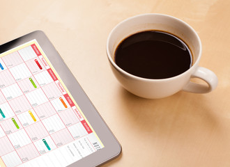 Tablet pc showing calendar on screen with a cup of coffee on a d