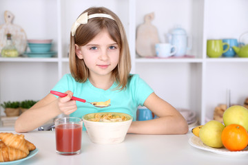 Beautiful little girl eating breakfast in kitchen at home