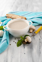 Mushroom soup in white pot, on napkin,  on wooden background