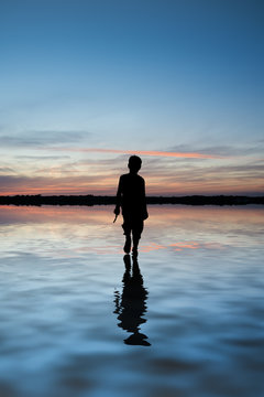 Concept image of young boy walking on water in sunset landscape