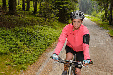 Naklejka premium Woman mountain biking through forest road