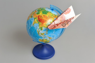 Globe with origami plane made from money on gray