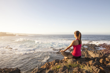 young woman practicing yoga meditation on the beach at sunset