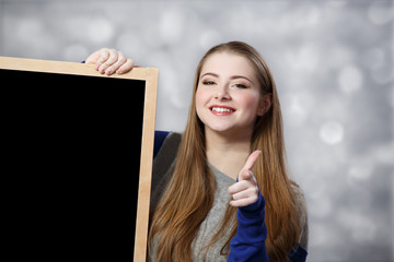 student holding a chalkboard points at you at light background