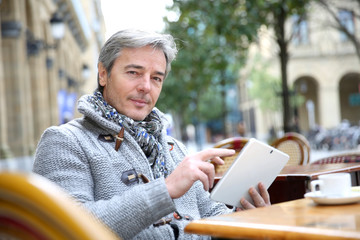 Obraz premium Mature man sitting at coffee shop table with tablet