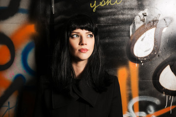 Young woman in black coat at the grunge graffiti wall