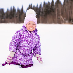 Little happy adorable girl sitting on the snow at winter sunny