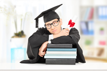 Worried college graduate leaning on stack of books, indoors