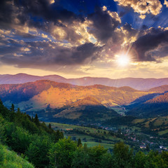 Fototapeta na wymiar village on hillside meadow with forest in mountain at sunset