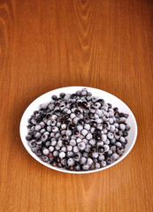 heap of frozen black currant in a plate on the wooden surface