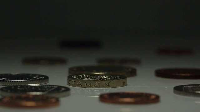 British One Pound coin spins amidst other UK currency coins